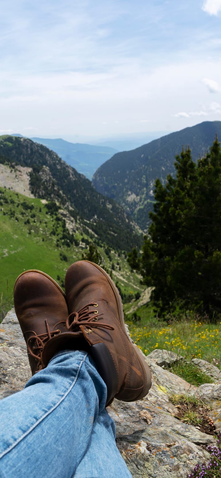 Ausgestreckte Beine auf einem Felsen, davor ein weites Bergtal.
